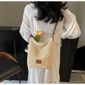 Détail d'un sac seau au crochet crème avec bandoulière en cuir brun et étiquette