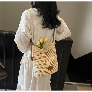 Détail du sac seau tissé ajouré beige avec lanières en cuir marron et perle rouge