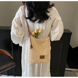 Détail du sac seau en tricot ajouré avec écusson en cuir et bandoulière à perles brunes