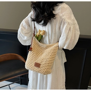 Détail du sac seau en tricot ajouré avec un écusson en cuir brun et texture tissée