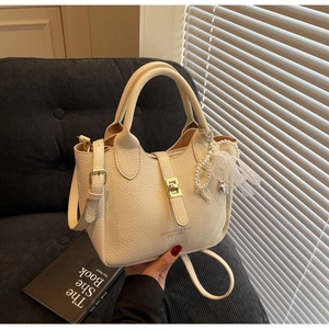 Close-up of beige lychee grain leather bucket bag with pearl charm and lace bow detail