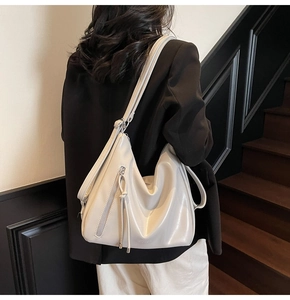 Detail of minimalist cream hobo bag showing side zipper and knot tassel texture