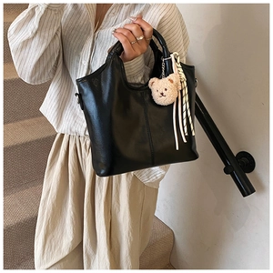 Detail of black matte leather bucket bag with cute bear charm and striped knot decoration