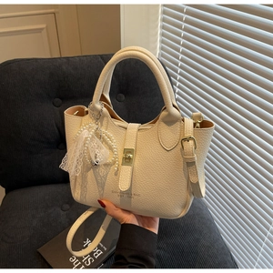 Detail view of off-white lychee leather bucket bag with gold lock and pearl charm