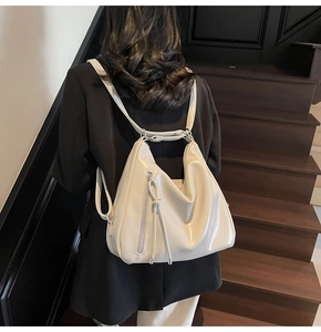 Detail of minimalist cream leather backpack featuring a long fringe tassel zipper pull