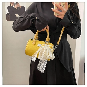 Mirror selfie showing yellow woven Boston bag with pearl lace bow charm on black dress