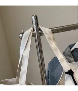 Close-up of white canvas tote bag with black ties hanging on a metal rack in a studio