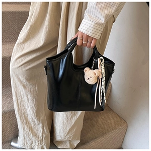 Close-up of black leather bucket bag with cute bear charm and striped knot detail