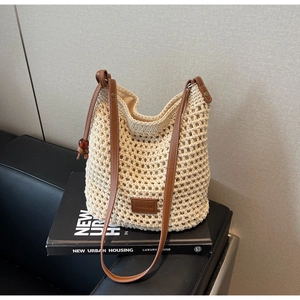 Détail du sac seau en tricot évidé avec bandoulière en cuir brun sur un canapé noir
