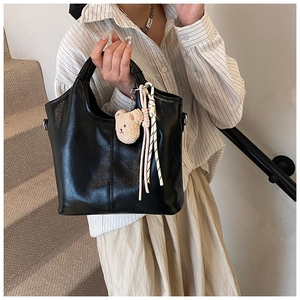Detail view of a black glossy PU leather handbag with cute bear charm and woven rope accent
