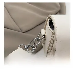 Detail of silver metal lobster clasp and beige leather strap on crossbody saddle bag
