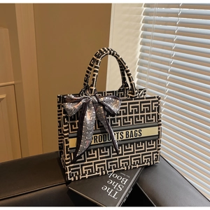 Close-up of geometric jacquard tote bag featuring central logo band and black silk bow