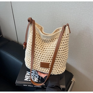 Détail de la maille et de la bandoulière en cuir d'un sac seau au crochet beige sur canapé