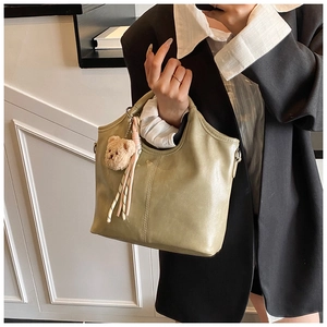 Detail view of light green PU leather bucket bag with plush bear charm and ribbon