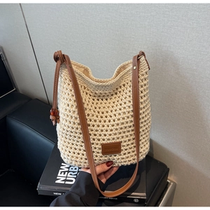 Gros plan du sac seau en crochet beige avec bandoulière en cuir et patch de marque