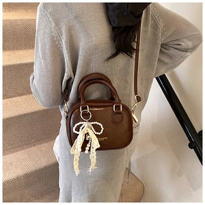 Dettaglio borsa a tracolla in pelle marrone vintage con ciondolo a fiocco di perle