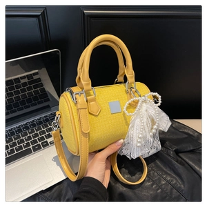 Detail of yellow cylindrical handbag featuring woven texture and lace pearl bow charm