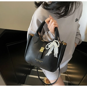 Close-up of black lychee grain leather bucket bag with lace bow and gold metal buckle