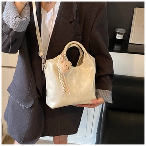 Detail of creamy white bucket bag with soft leather texture and plush bear pendant
