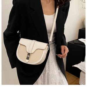 Detail of a beige saddle crossbody bag featuring a unique woven straw texture and metal lock