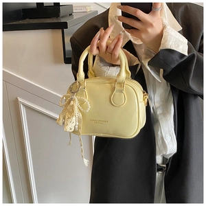 Dettaglio mini borsa Boston in pelle lucida gialla con ciondolo a fiocco di perle e manici