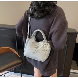 Close-up of light grey-blue bucket bag with lace bow and pearl heart charm detail