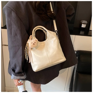Detail of a beige bucket bag with a plush bear charm and striped ribbon on a model