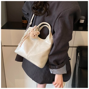 Detail of cream white bucket bag with a cute plush bear charm and striped ribbon accent