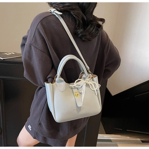 Detail of light blue pebbled leather bucket bag with pearl bow charm and gold hardware