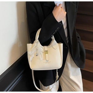 Detail of cream bucket bag with litchi texture, pearl bow charm and heart pendant