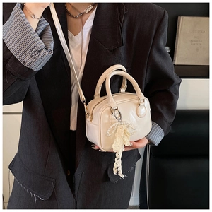 Dettaglio di una mini borsa Boston bianco crema con ciondolo decorativo a fiocco di pizzo e perle