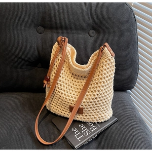 Gros plan du sac seau au crochet beige avec bandoulière en cuir brun et logo