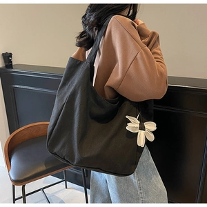 Detail of a large black canvas tote bag with a white flower charm worn by a model