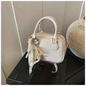 Dettaglio borsa in pelle crema con ciondolo di perle e finiture in metallo dorato