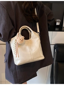 Elegant cream PU bucket bag with round handle and cute bear charm in lifestyle setting