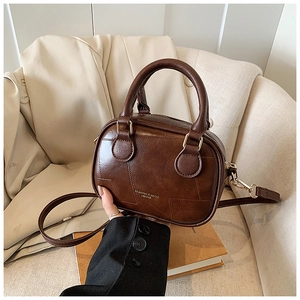 Dettaglio della borsa Boston in ecopelle marrone scuro con finiture dorate su divano