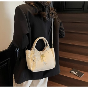 Detail of cream lychee leather bucket bag with gold hardware and decorative pearl bow