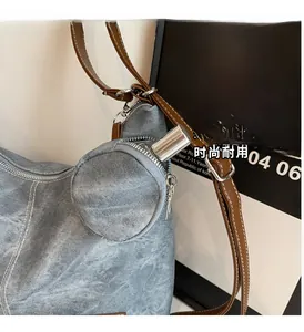 Detail of blue denim tote bag with brown leather strap and small circular zippered pouch