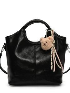 Elegant black leather bucket bag with plush bear charm shown on a pure white background