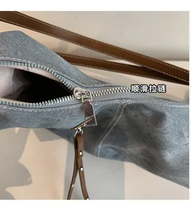 Detail view of a denim tote bag showing the smooth silver metal zipper and brown leather trim