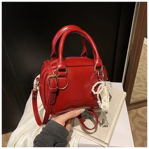 Dettaglio borsa rossa in vernice con logo dorato e ciondolo decorativo in pizzo e perle