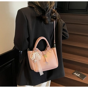 Pink lychee texture bucket bag with pearl lace bow charm shown on model in black suit