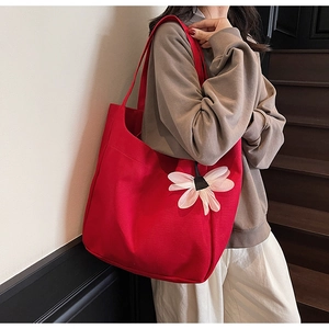 Detail of red canvas tote bag featuring a white 3D flower and reinforced shoulder strap