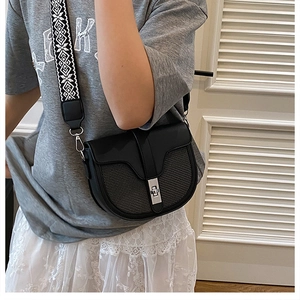 Detail of black saddle bag featuring mesh texture, silver buckle, and woven strap