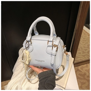 Dettaglio mini borsa in pelle azzurra con finiture dorate e ciondolo a fiocco di perle