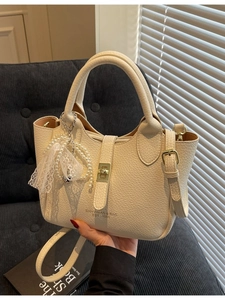Elegant cream bucket bag with litchi texture and pearl charm on a blue chair