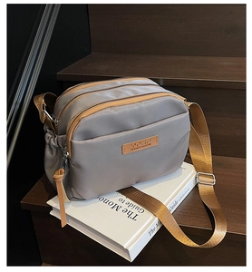 Close-up of grey crossbody bag with three zipper compartments and brown shoulder strap