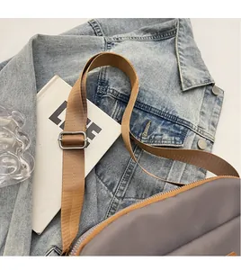 Detail of adjustable wide brown nylon strap with silver buckle on a gray crossbody bag