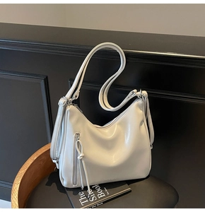 Cream white shoulder bag with zipper fringe and dual straps on a designer chair
