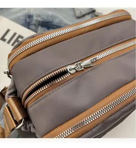Macro shot of smooth dual silver zippers and nylon fabric detail on a grey crossbody bag
